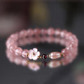 Women's strawberry quartz peach blossom crystal bracelet with floral design on wrist.