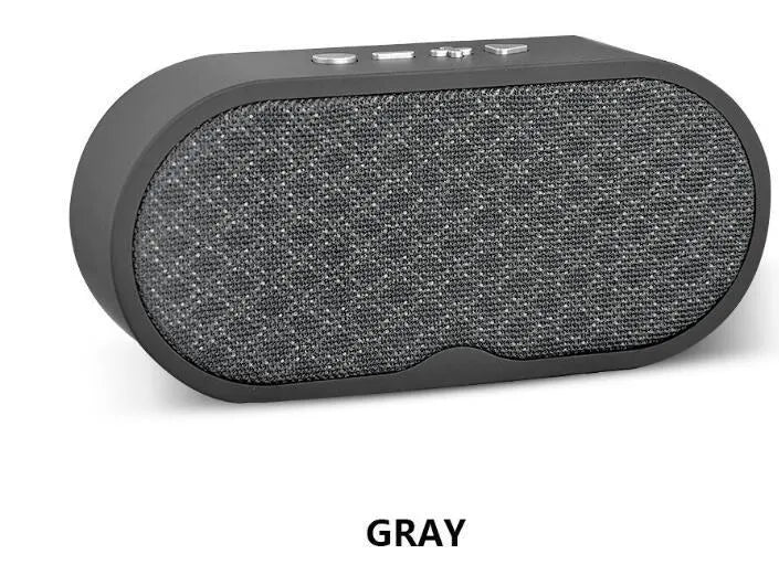 Grey portable Bluetooth speaker with subwoofer, HD microphone, TF card slot and USB port on a table.