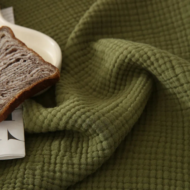 Four-layer cotton gauze blanket with tassel trim shown in avocado green colour.