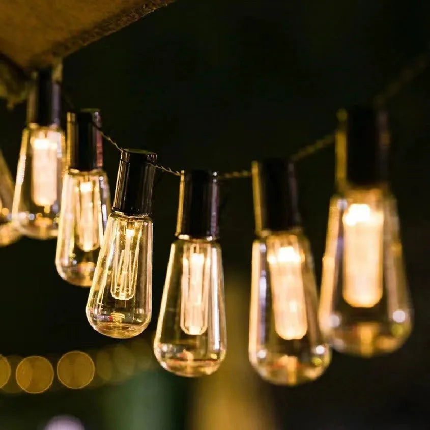 Outdoor retro string lights with glass infusion bottle bulbs hung along a black wire.