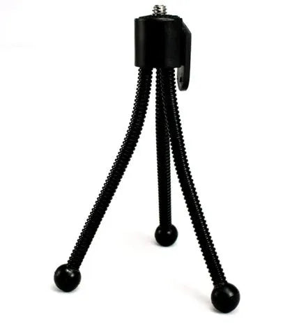 Small black iron mini tripod with ball head, shown collapsed to 110mm and extended on a desktop next to a smartphone.