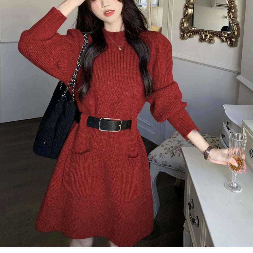 A woman wearing a long sleeve, loose knitted dress in a high-waist style with a black belt.