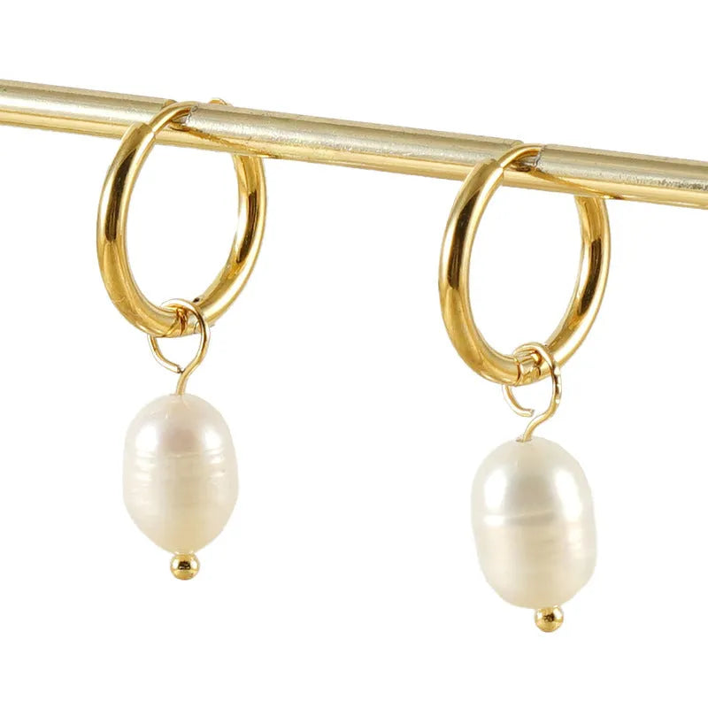 A pair of gold-coloured geometric stud earrings with a central white pearl on a white background.