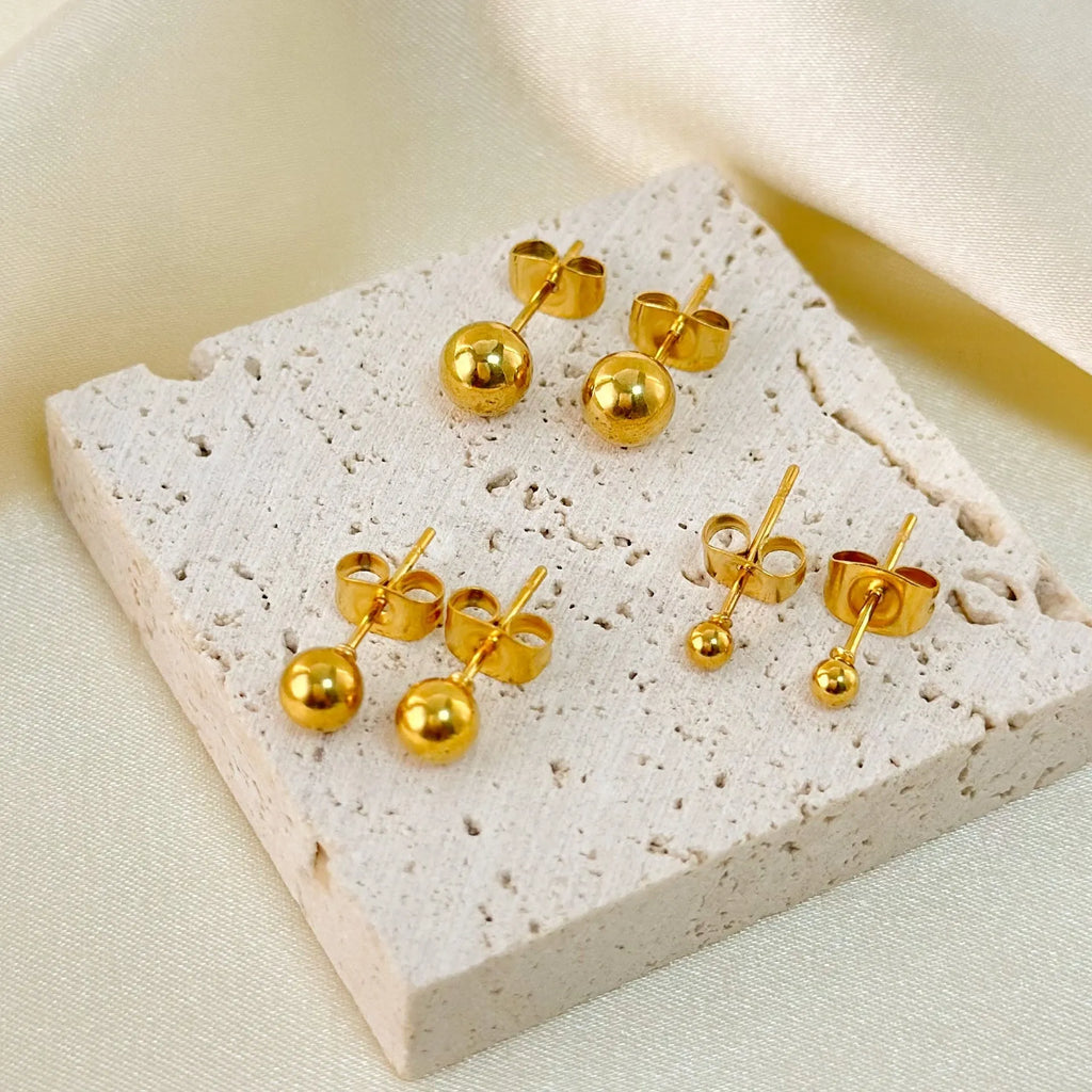 Minimalist round ball stud earrings in gold and silver finishes, showing different size options on a plain background.