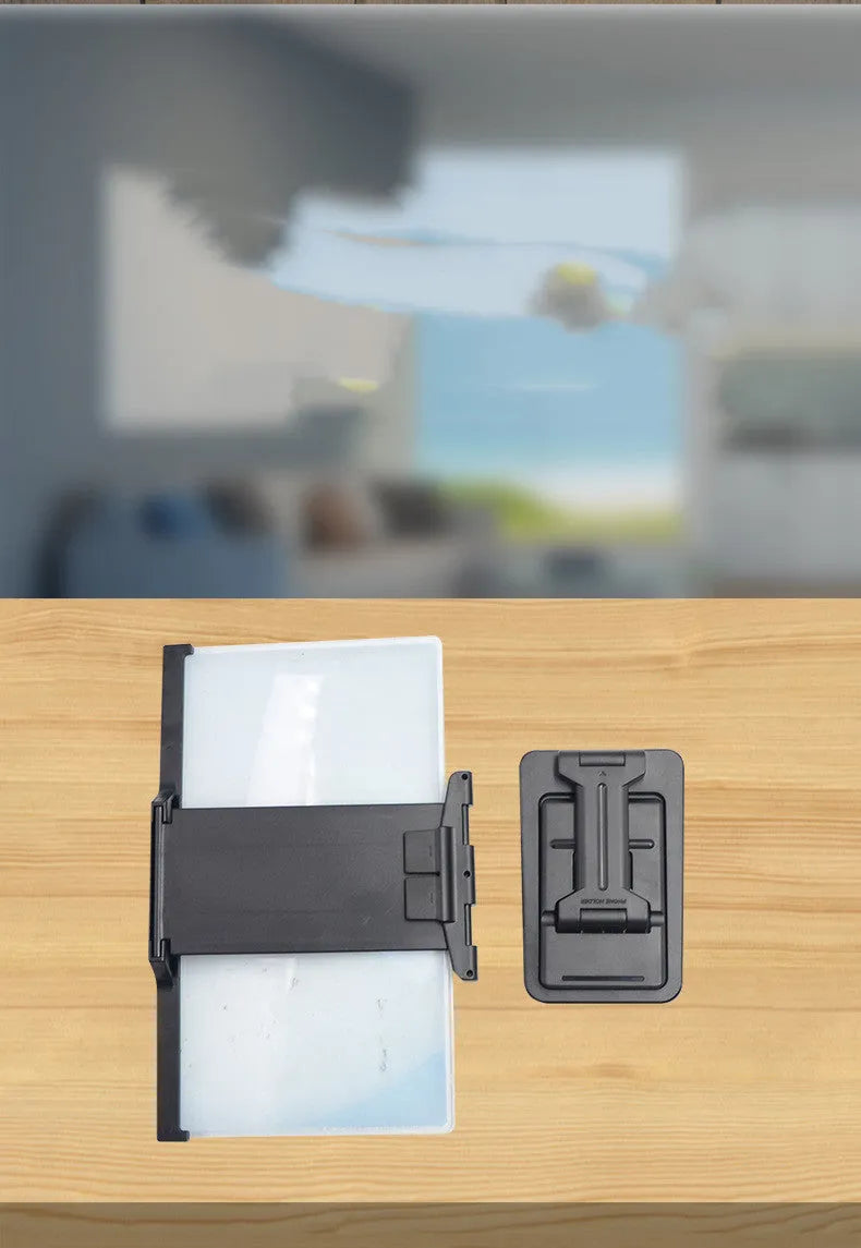 Black folding mobile phone screen magnifier with detachable holder on a desk.