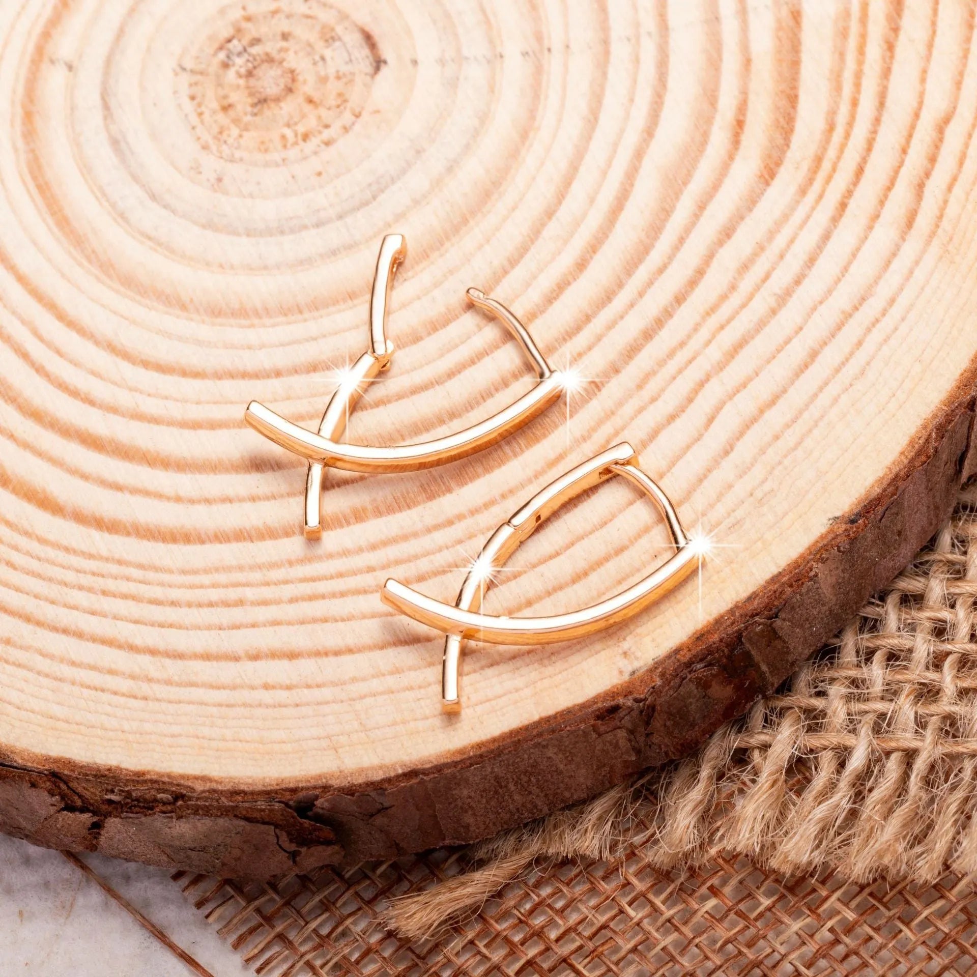 A pair of rose gold coloured cross shaped copper earrings on a plain background.