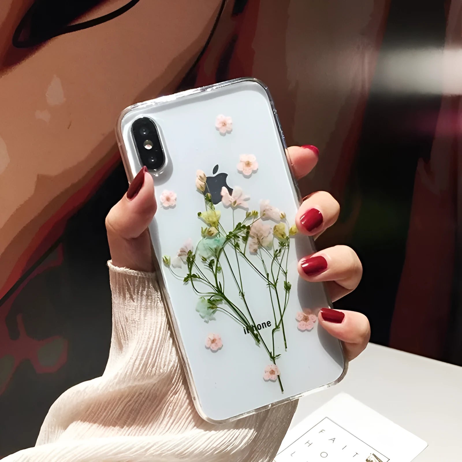 Clear handmade TPU iPhone case with pink dried flowers encased in epoxy resin on the back.