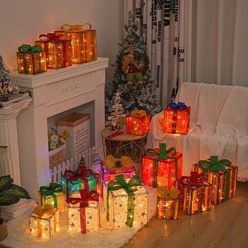 Set of three glittering pre-lit Christmas gift boxes with red bows, illuminated with warm white LED lights outdoors.