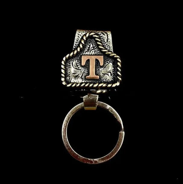 Handmade cow tag shaped metal keychain with a brown leather attachment strap.