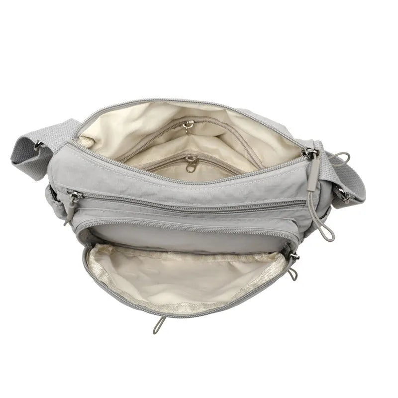 Soft grey nylon crossbody bag with an external pocket and adjustable shoulder strap.