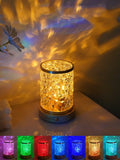 Small rotating water ripple night light with a solid wood base and acrylic body on a bedside table.