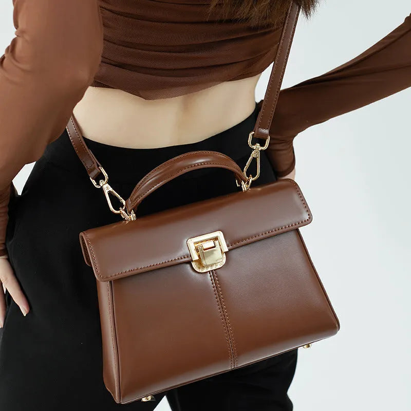 Black leather women's shoulder bag with vachette clasp, shown open to reveal internal zippered pocket.