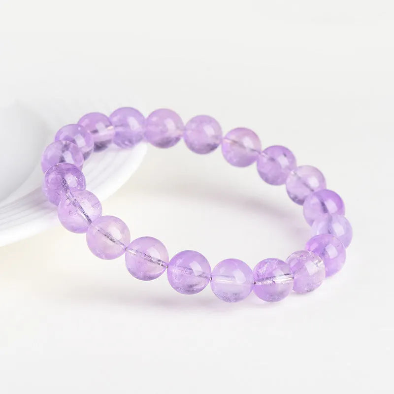 Lavender coloured amethyst crystal bracelet with round beads and a geometric water ripple design on a wrist.
