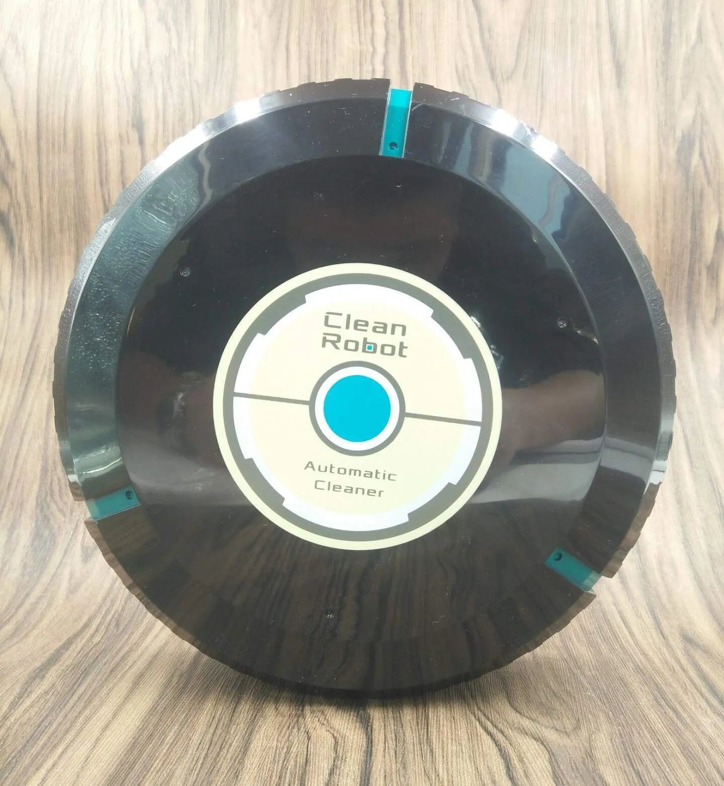 Black automatic sweeping robot cleaner on a wooden floor.