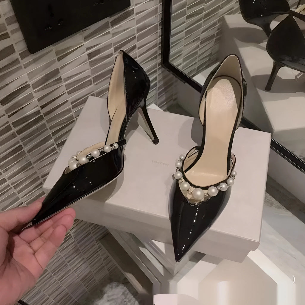 Women's black patent leather stiletto high heels with a pointed toe and pearl decoration on the upper.