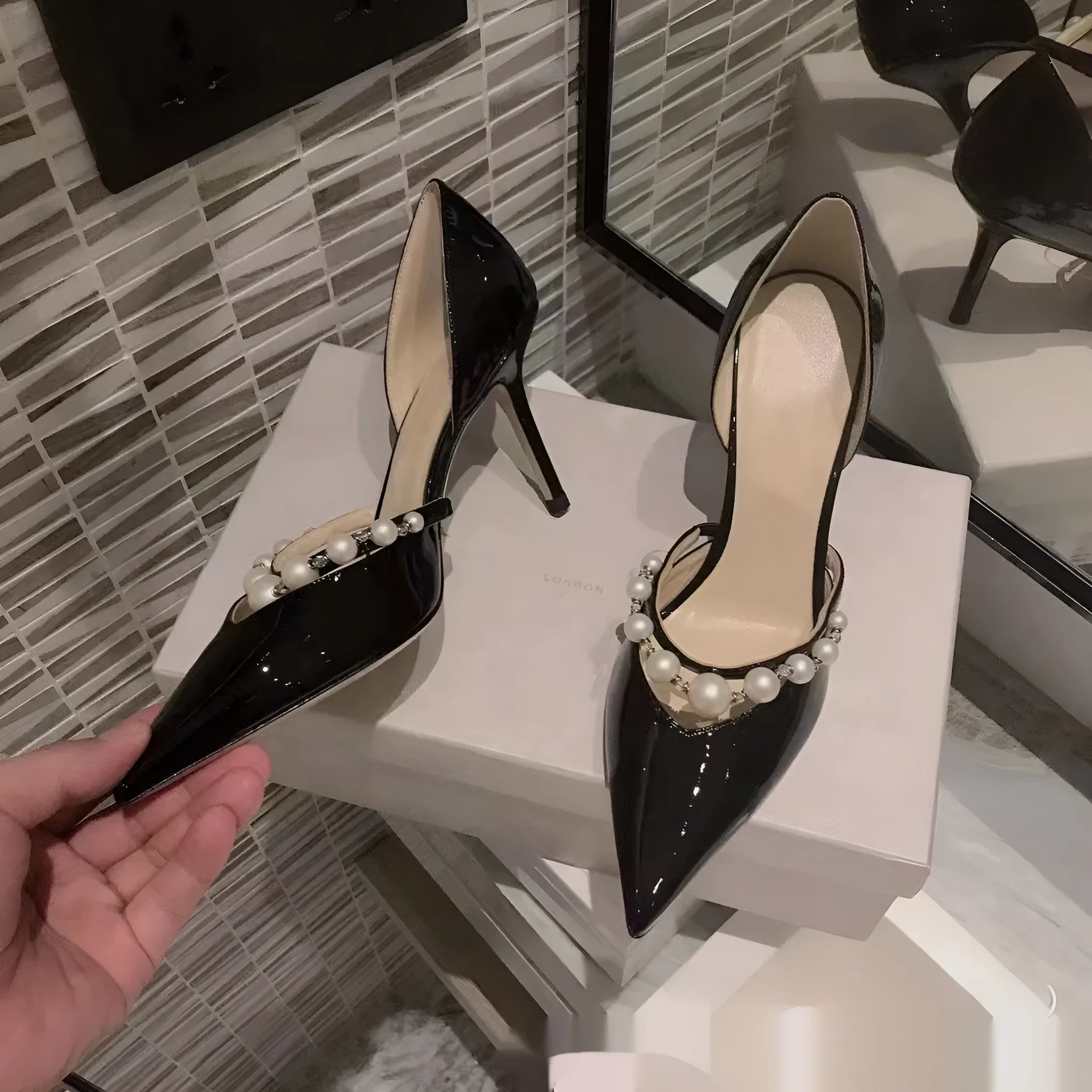 Women's black patent leather stiletto high heels with a pointed toe and pearl decoration on the upper.