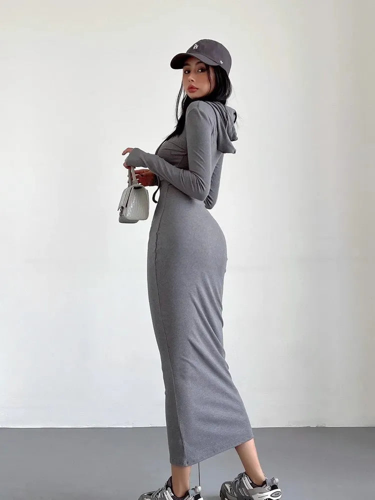 A woman wearing a light grey, long-sleeve polyester sheath dress with an over-the-knee length and high waist.