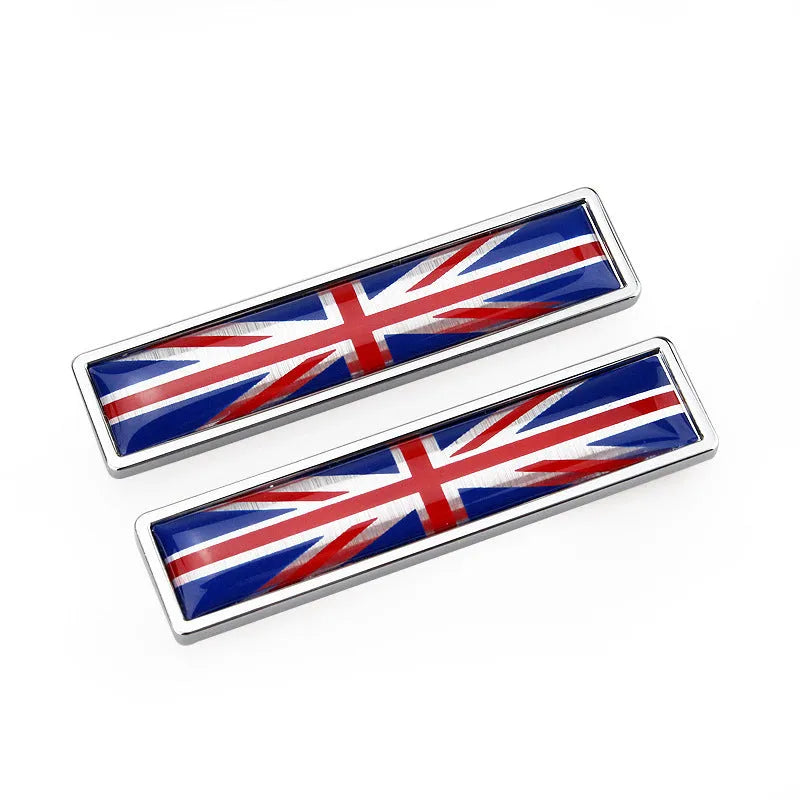 A pair of silver zinc alloy car badge labels with coloured national flag designs, shown at 58mm by 14mm scale.
