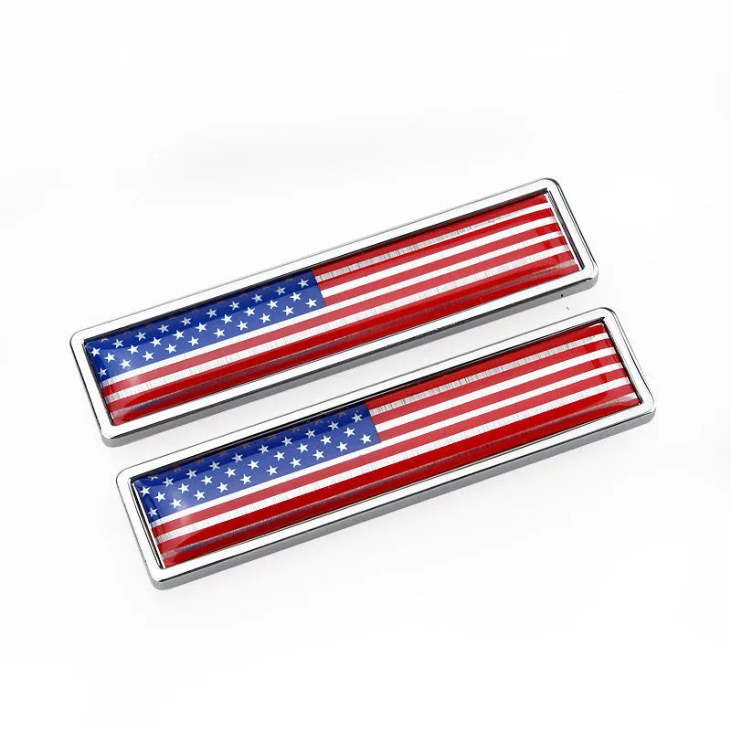 A pair of silver zinc alloy car badge labels with coloured national flag designs, shown at 58mm by 14mm scale.