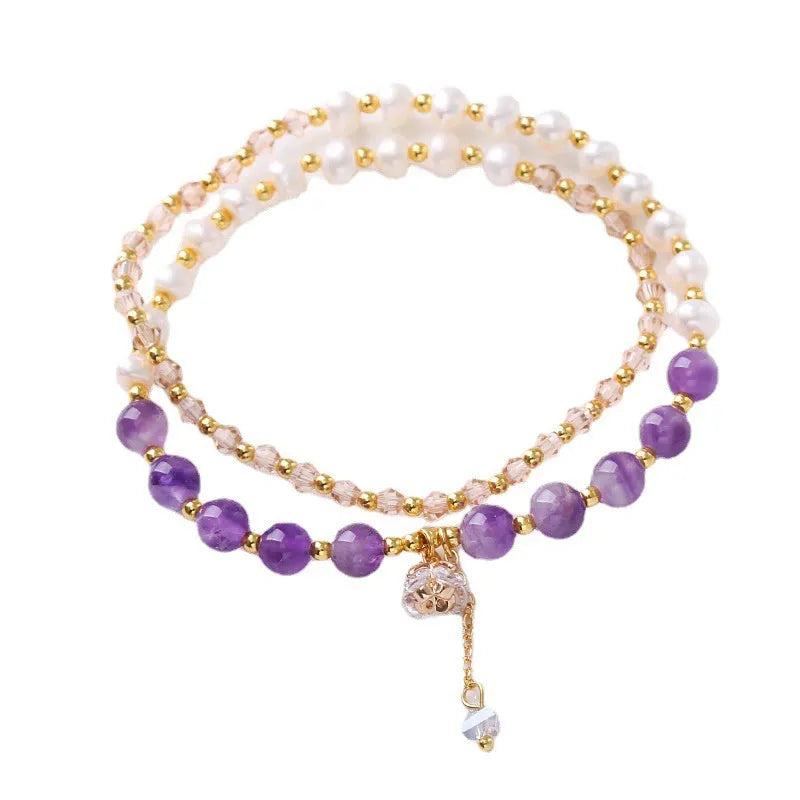 Close-up of a women's double ring bracelet with a freshwater pearl and amethyst crystal beads on a wrist.