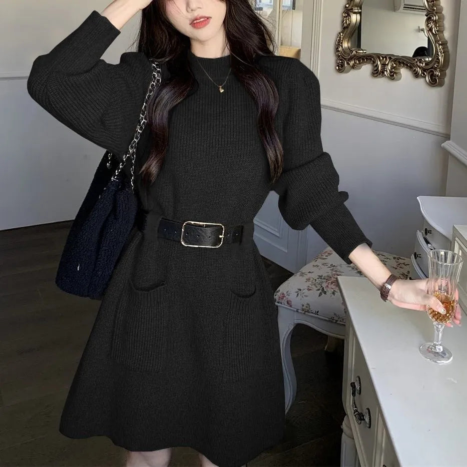 A woman wearing a long sleeve, loose knitted dress in a high-waist style with a black belt.