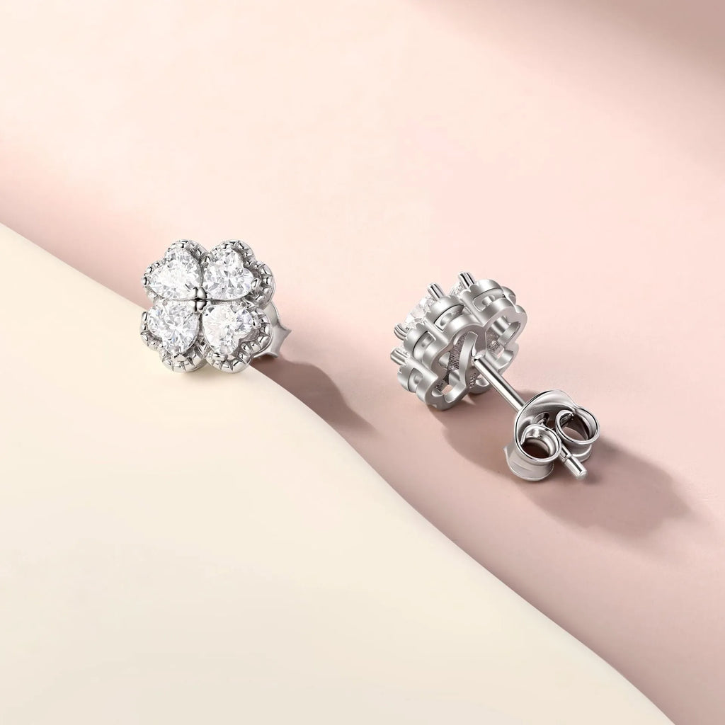 Close-up of a pair of heart-shaped 925 silver earrings with a four-leaf clover charm and zircon stones, in white gold colour.