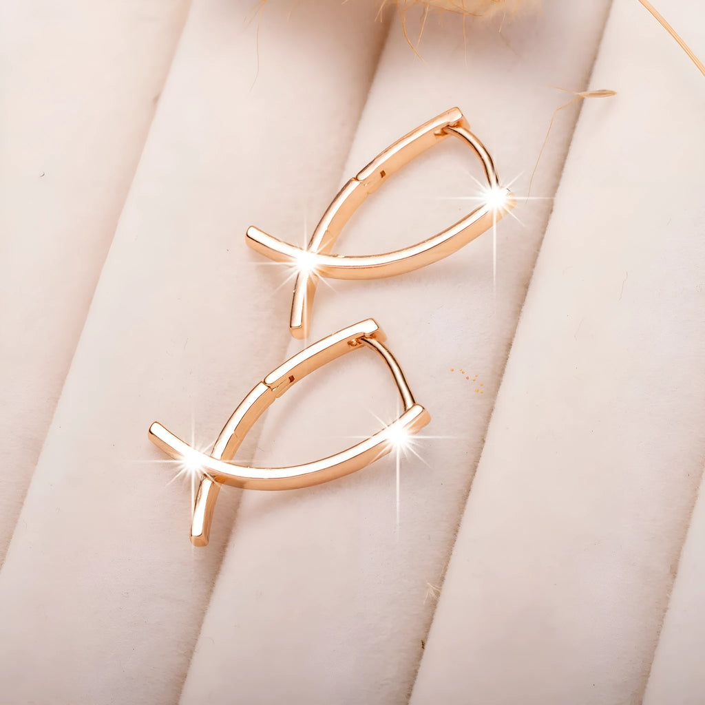 A pair of rose gold coloured cross shaped copper earrings on a plain background.