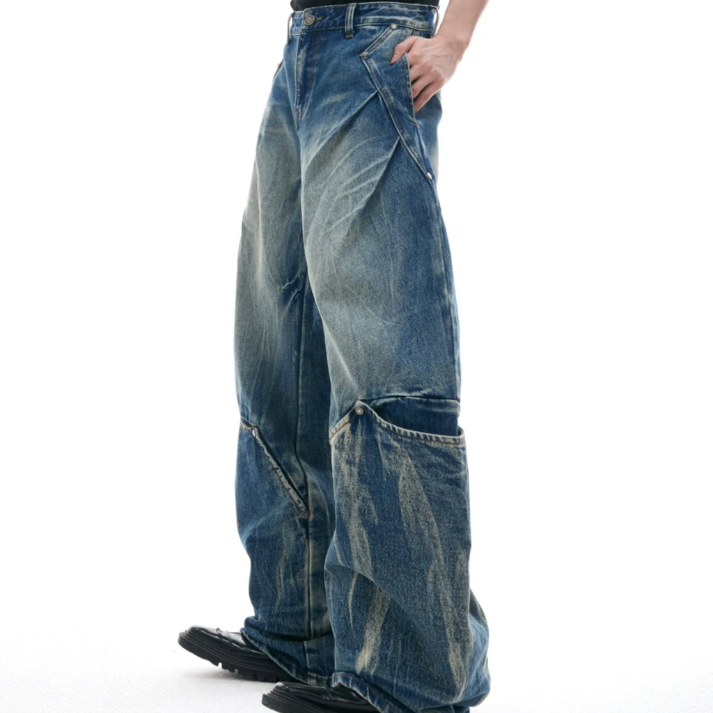 Man wearing loose fit verdant blue retro jeans with a curved knife cut and washed burst pattern.