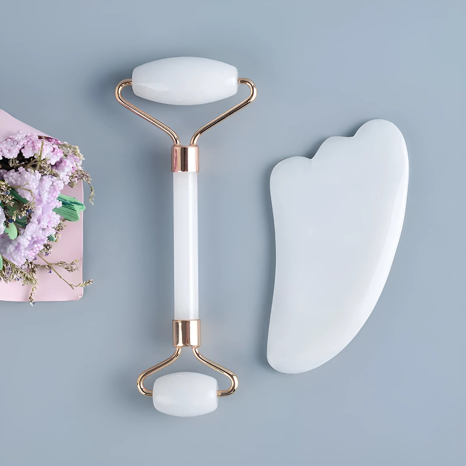 White jade facial roller and gua sha scraper tools placed on a smooth wooden storage board.