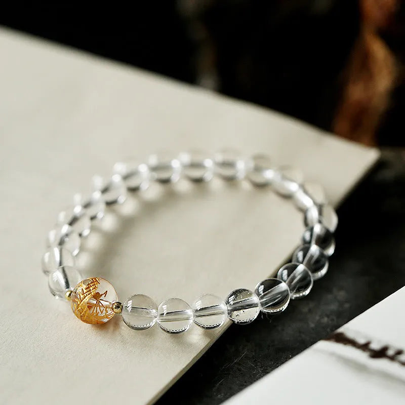 Geometric obsidian and white crystal bracelet with a golden dragon charm on a wrist.