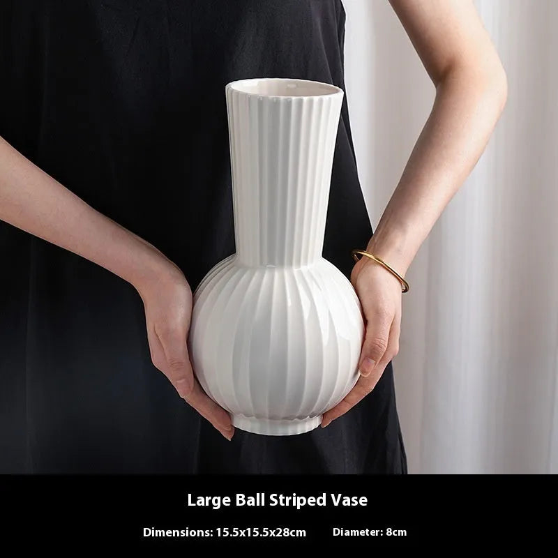 White ceramic ball vase with blue stripes and artificial blue orchid stems on a wooden table.