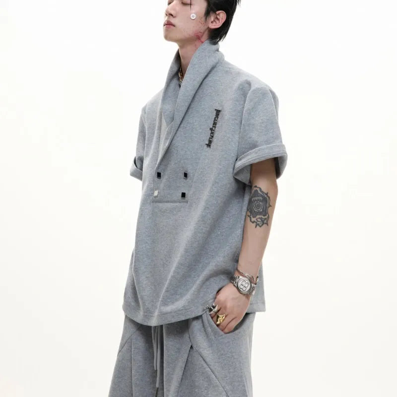 Men's dark grey cotton sports suit with V-neck short sleeve top, padded shoulders, metal embellishments, and matching shorts.