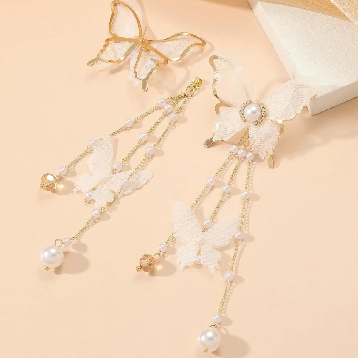 A pair of white butterfly-shaped earrings with tassels, lace details, pearls, and rhinestones.