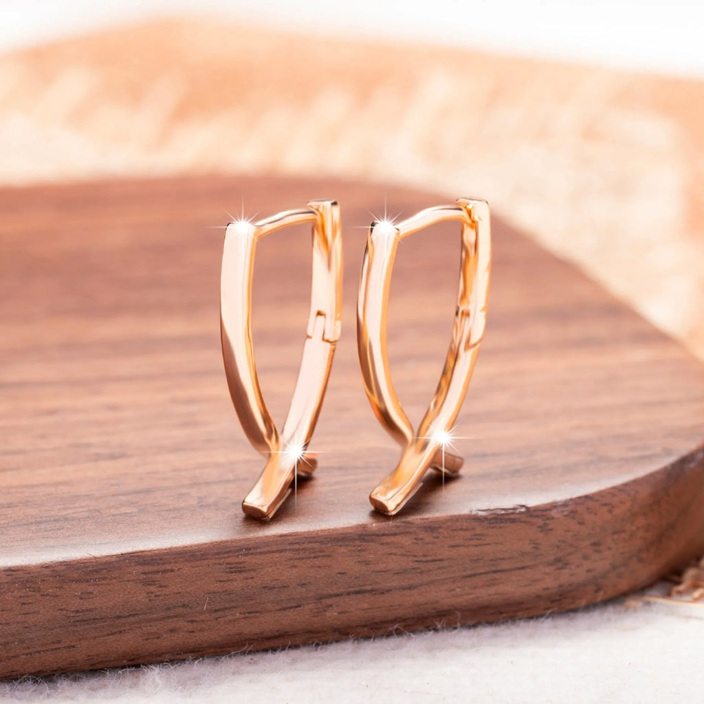 A pair of rose gold coloured cross shaped copper earrings on a plain background.