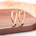 A pair of rose gold coloured cross shaped copper earrings on a plain background.