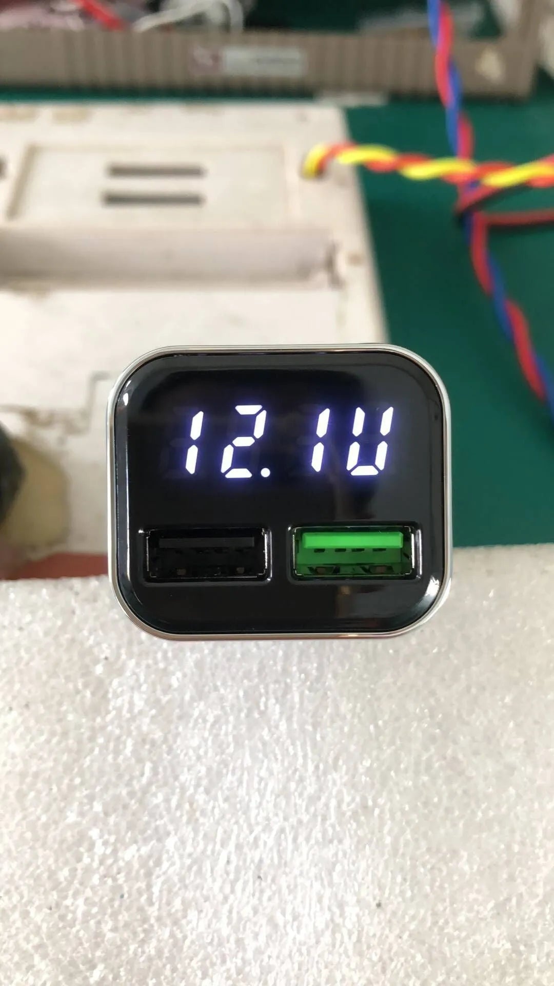 Black car charger with digital display showing voltage and current readings, dual USB ports