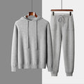 Man wearing a light grey cashmere hooded sweatshirt and matching trousers, a casual winter two-piece set.
