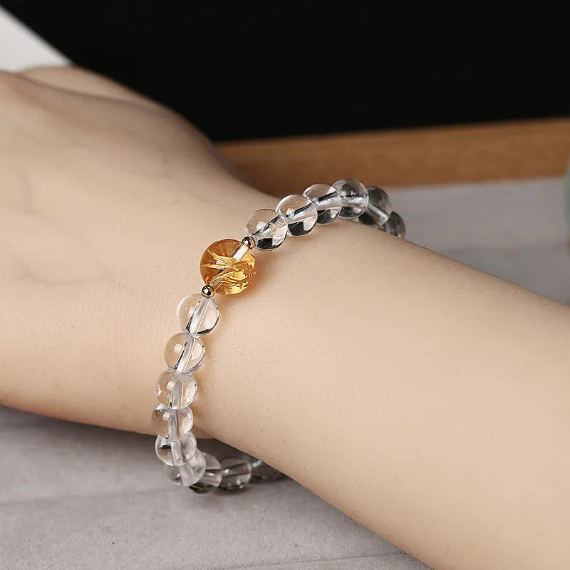 Geometric obsidian and white crystal bracelet with a golden dragon charm on a wrist.