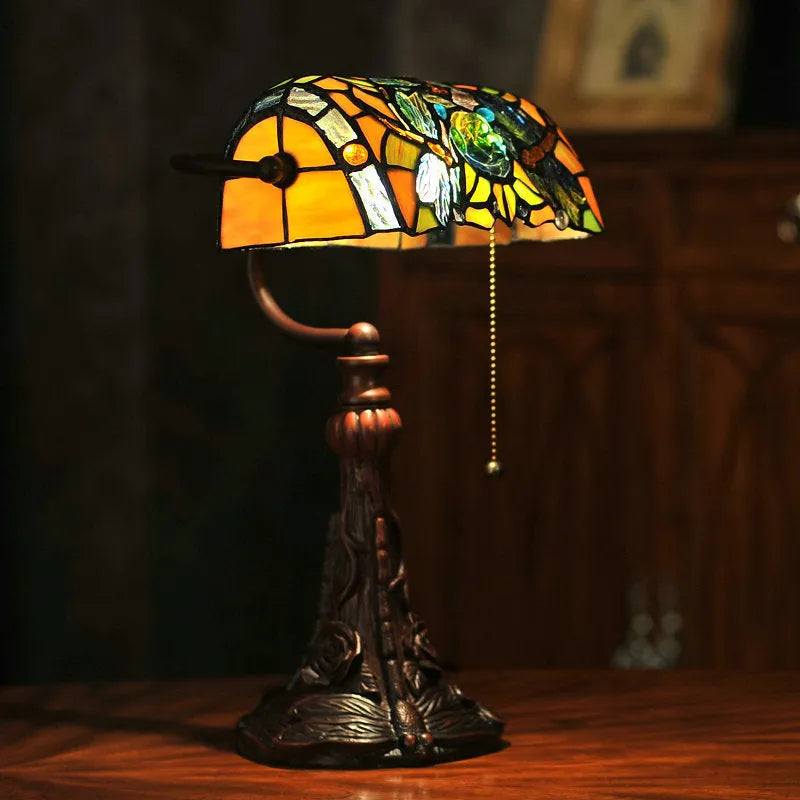 Tiffany stained glass table lamp on a desk, showing its coloured shade and resin base.