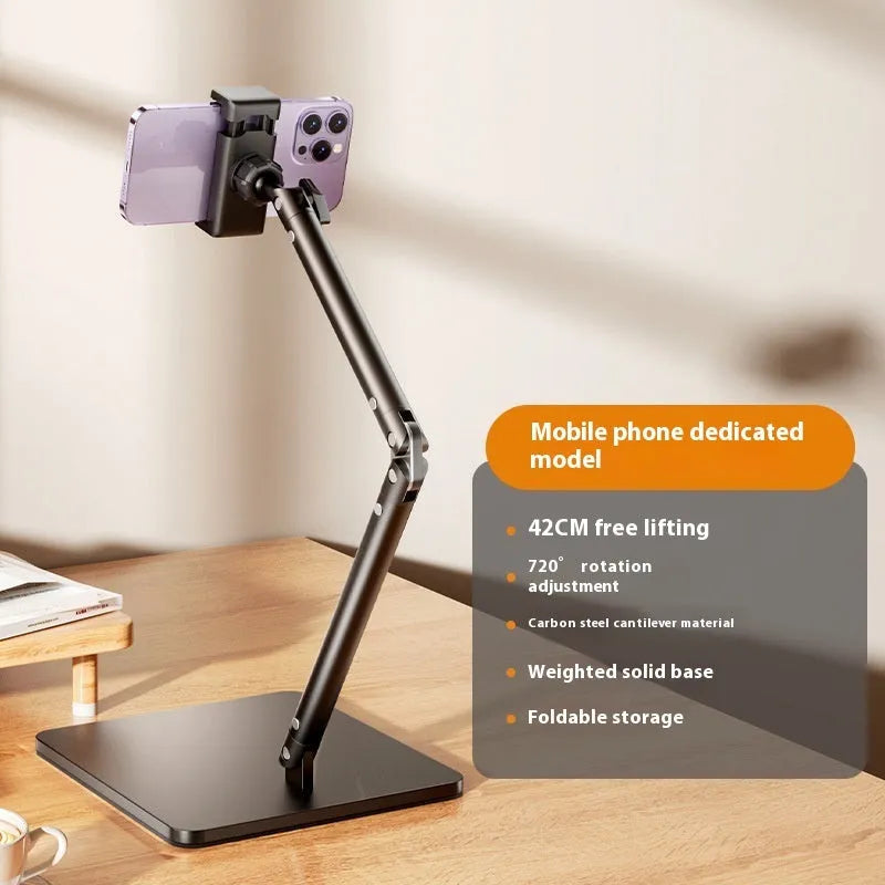 Silver alloy desktop phone bracket with double arms holding a smartphone, shown with a remote control on a wooden desk.