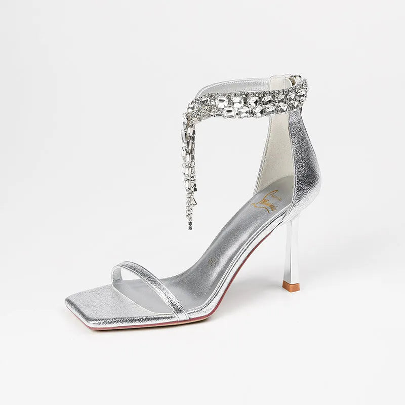 Women's silver high heel sandals with ankle buckle strap and square open toe on a plain background.