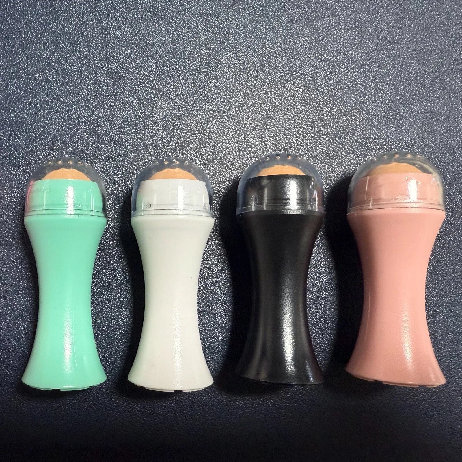 Portable volcanic stone facial roller for oil control, shown in choice of black, green, pink, or white.