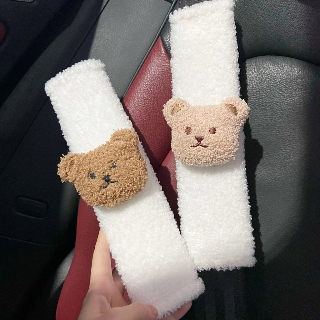 Plush cartoon bear car seat belt shoulder cover in khaki colour, shown next to a car seat.