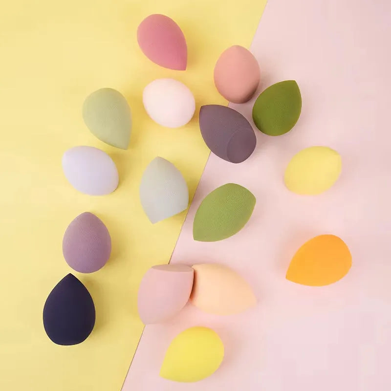 Set of seven differently shaped makeup sponges in various colours on pink background