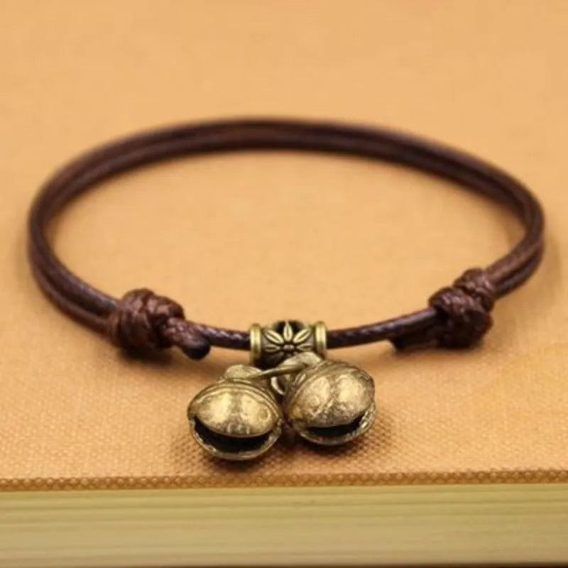 Black nylon rope dog collar with a shiny brass bell on a wooden surface.