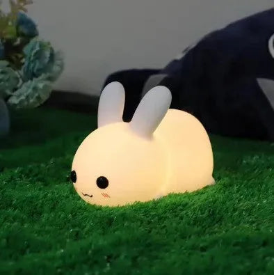 White silicone rabbit night light with warm and white LED glow on a wooden bedside table