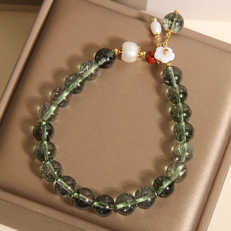 Green phantom quartz crystal bracelet with small shell flower design on woman's wrist.
