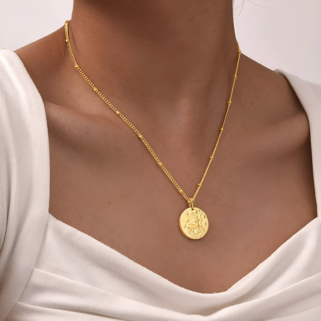 Stainless steel zodiac necklace with round pendant showing embossed constellation design on a cross chain.