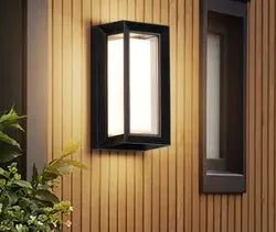 Waterproof IP65-rated outdoor wall lamp with aluminium body and acrylic shade, shown in a garden setting.