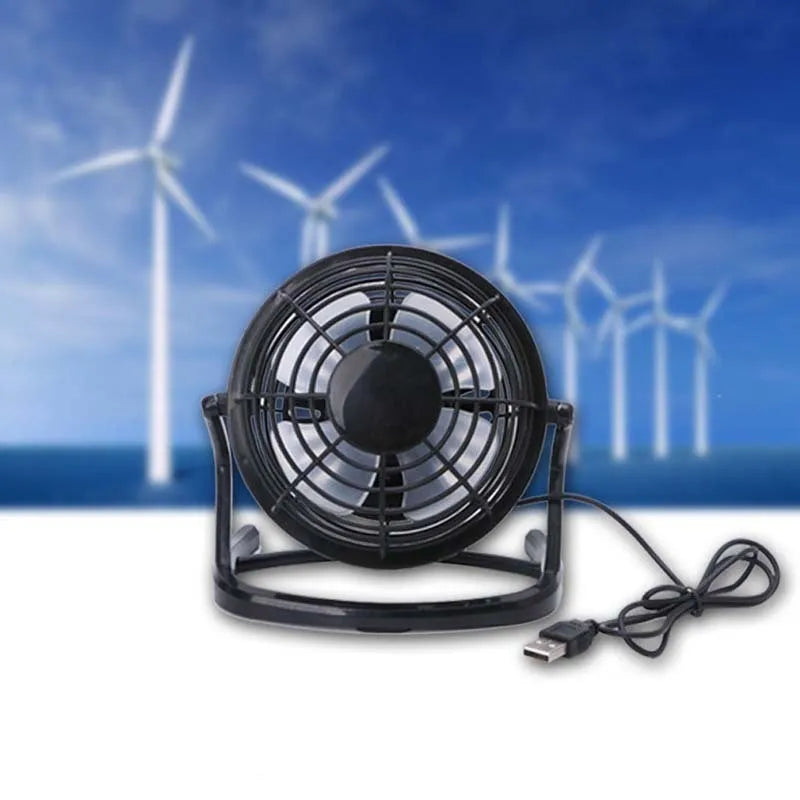 Mini black USB desk fan with adjustable tilt angle on a wooden desk next to a laptop.